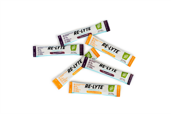 Several single-serving packets of Re-Lyte Immunity electrolyte powder in Blackberry and Pineapple Orange flavors lay scattered on a white surface.