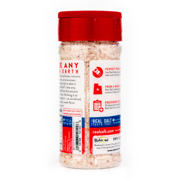 Clear shaker filled with Redmond Real Salt, showcasing the product's unrefined, coarse texture and natural pink hue.