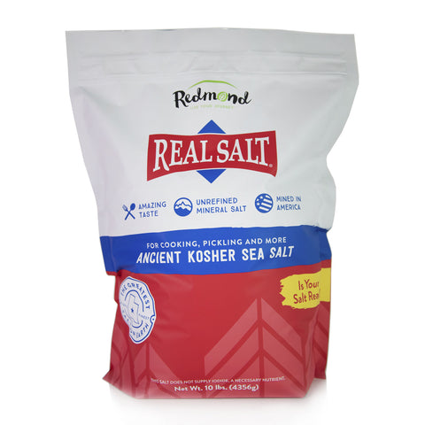 A white bag of Redmond Real Salt, Ancient Kosher Sea Salt, stands upright against a white background. The bag highlights the salt's amazing taste, unrefined mineral content, and American origin. 
