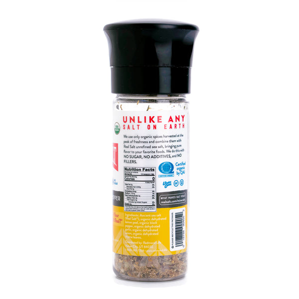 A clear glass grinder filled with Real Salt's organic lemon pepper seasoning sits against a white background. 

