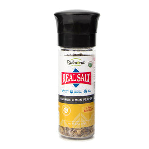 Redmond Real Salt Organic Lemon Pepper grinder features a black lid and displays the brand and product name with a transparent section revealing the seasoning. 
