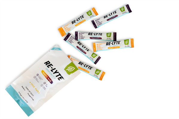 Six single-serving stick packs of Re-Lyte Immunity electrolyte powder in Blackberry and Pineapple Orange flavors spill out of a sample pack. 
