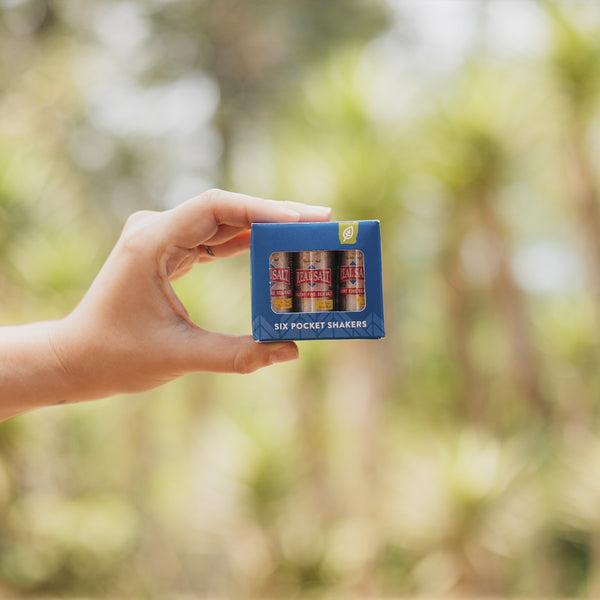 Hand holds up a box of six pocket-sized Real Salt shakers against a blurred green background. 
