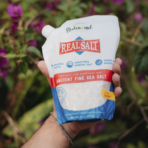 Hand holds a pouch of Redmond Real Salt, showcasing the unrefined, ancient sea salt mined in America. 
