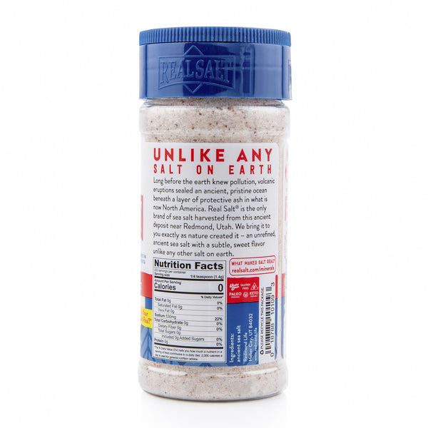 A clear shaker displays Real Salt, showcasing its natural, unrefined state with a subtle pink hue. The blue lid pops against the white label, emphasizing the brand's commitment to pure, ancient sea salt.