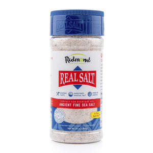 A clear plastic shaker of Redmond Real Salt Ancient Fine Sea Salt sits against a white background.