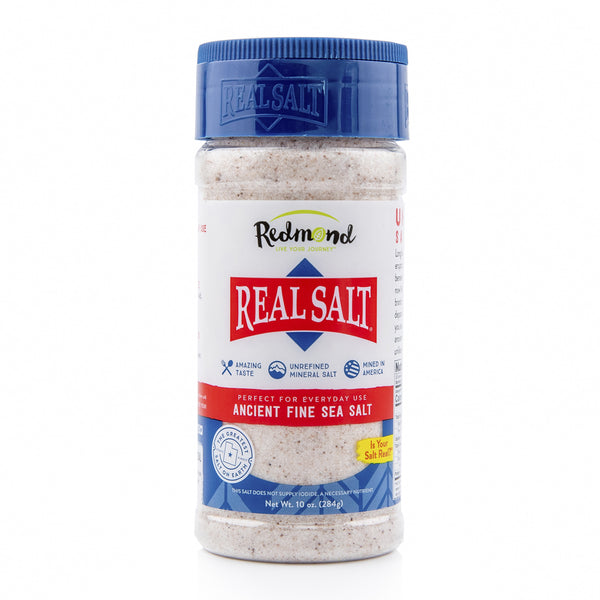 A clear plastic shaker of Redmond Real Salt Ancient Fine Sea Salt sits against a white background.