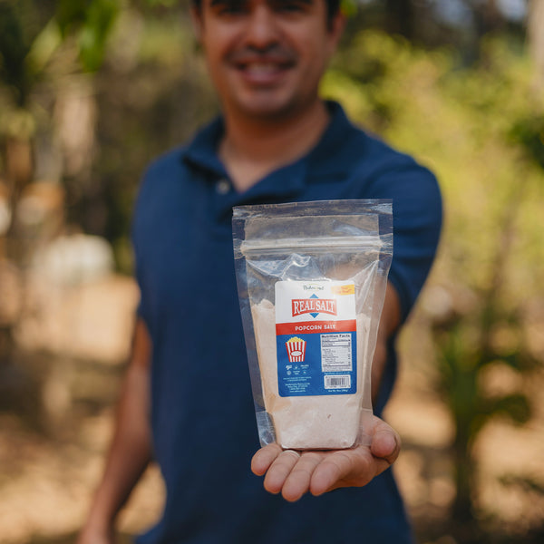 Man holds out a bag of Redmond Real Salt Popcorn Salt. 

